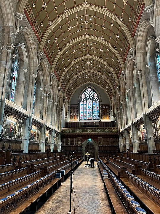 Grand chapel interior with high vaulted ceilings, stained glass windows, and long rows of wooden pews.