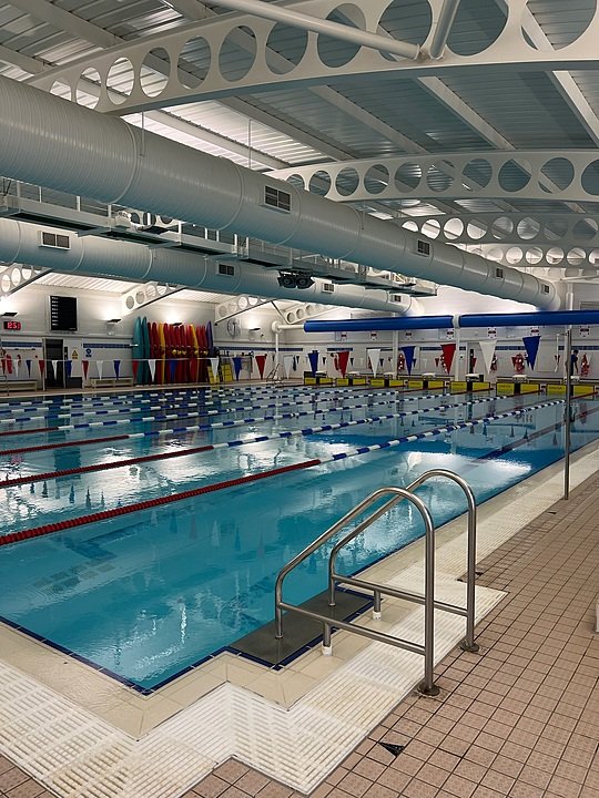 Indoor swimming pool with swimming lanes, colourful flags, and neatly arranged kayaks along the wall.