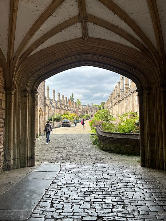 Cobblestone passageway framed by an arched stone entrance leading to a courtyard lined with historic buildings.