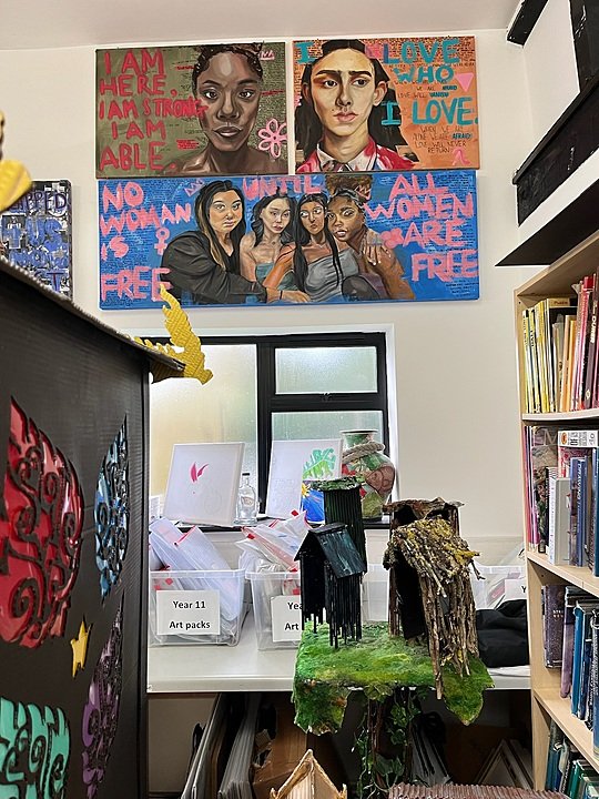 A room with art projects on the wall and a shelf with art books on the side