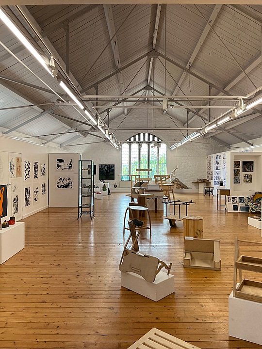 Bright exhibition room with wooden floors and student design projects displayed around the space.