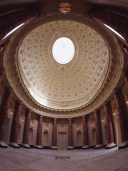 a stunning round marble saloon with pillars all around and beautifully decorated domed ceiling