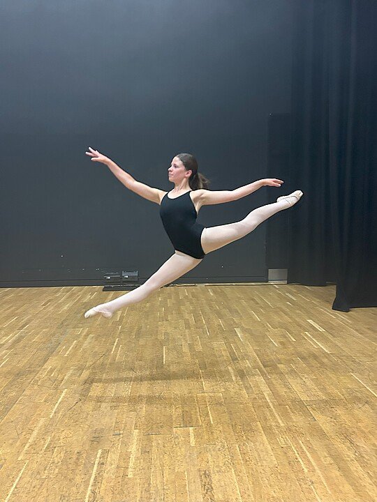 Ballet dancer in black ballet outfit mid-jump