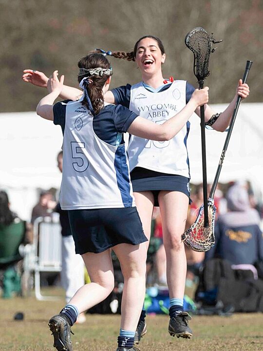 Two girls smiling happily, holding lacrosse rackets