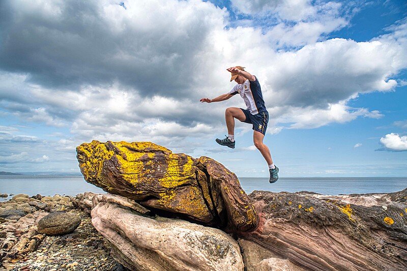 A student jumping over rocks by the sea