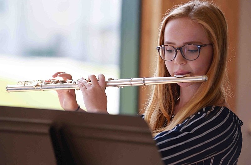 A girl with red hair and glasses playing the flute