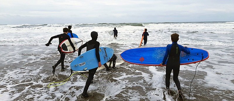 Children with surfboards and wetsuits running towards waves on a beach