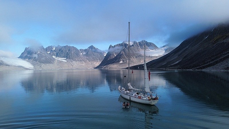 a white two-master in a fjord with snowy mountains in the background