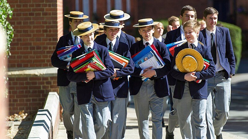 a group of students with their uniforms and hats carrying piles of books