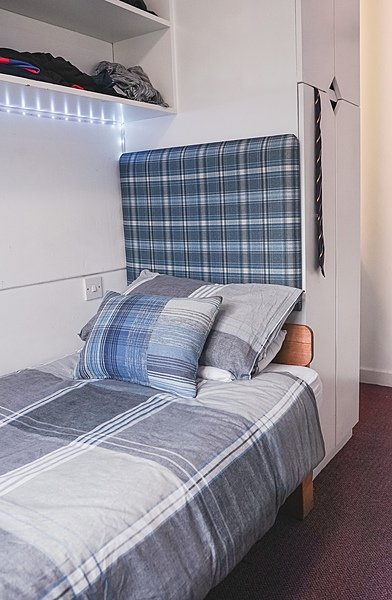 Neatly made boarding school bedroom with checkered bedding.