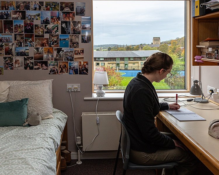 Girl sitting at a table in the process of writing with bed in the background