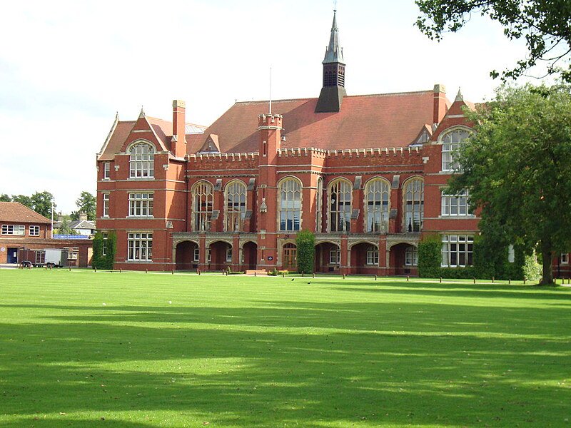 Large, red brick building with tall windows and a green lawn on a sunny day