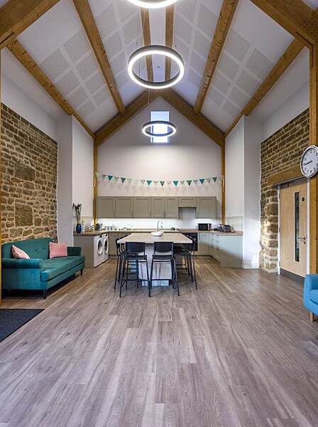 A bright modern kitchen and lounge with exposed brick walls, wooden beams, and circular ceiling lights.