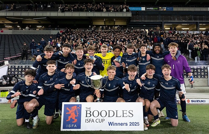 A boys’ football team celebrating with a trophy in front of a crowd after winning the Boodles ISFA Cup 2025.