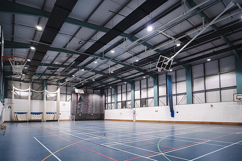 A spacious, modern sports hall with basketball hoops, a climbing wall, and marked courts for various indoor sports.