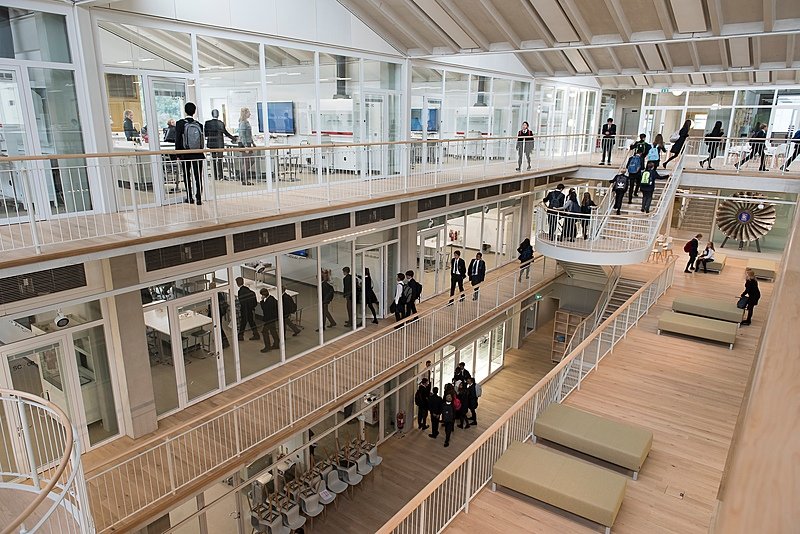 A bright, modern school building with open corridors, glass classrooms, and students walking between floors.