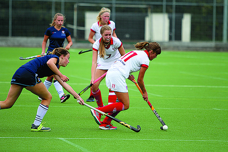 Girls’ field hockey match in progress on an outdoor pitch.