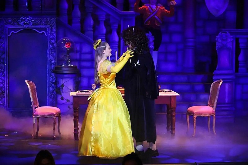 Girl in yellow ball gown and boy in black performing a dance on a theatre stage