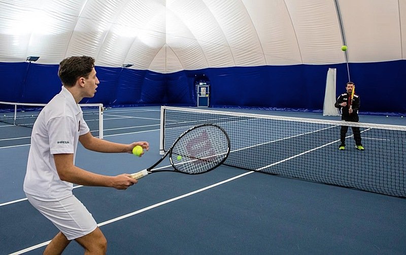 Two students playing tennis on a covered indoor sports court