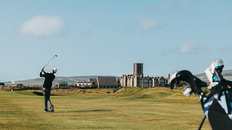 A pupil swinging a golf club on a golf course with King Williams College in the background