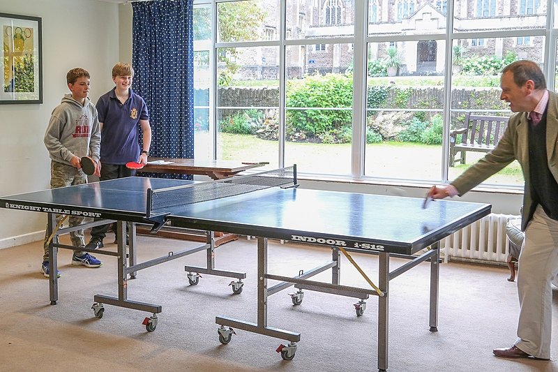 a teacher is playing table tennis against two of his students
