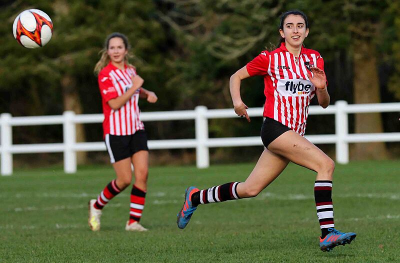 two female students outside playing football in their red and white striped jerseys