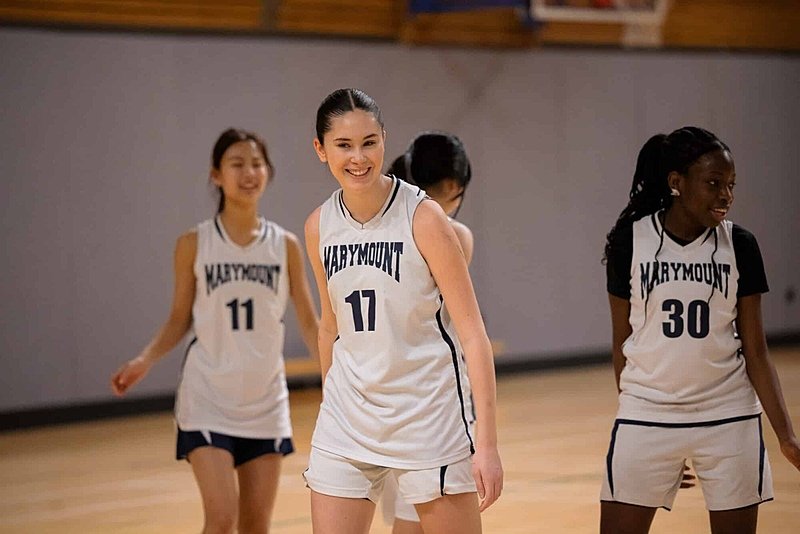 Four girls in basketball jerseys on a basketball court, smiling