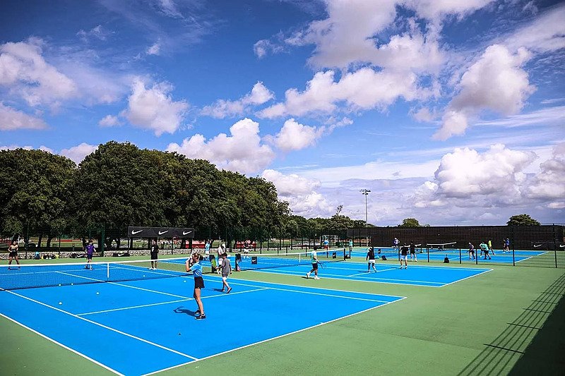 Pupils playing tennis on bright blue outdoor courts under a partly cloudy sky.