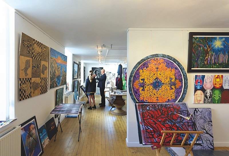 Room with different sized and shaped art exhibits on the walls with pupils inspecting some in the background