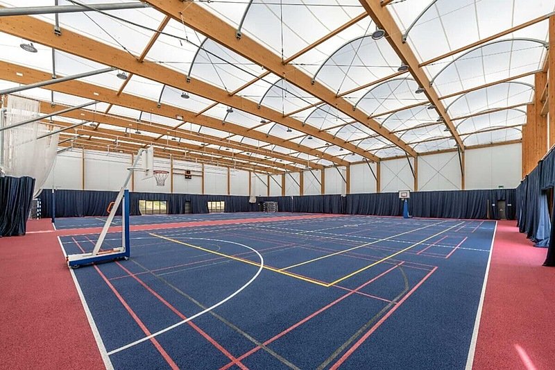 A brightly lit, modern sports hall with basketball hoops and cricket netting