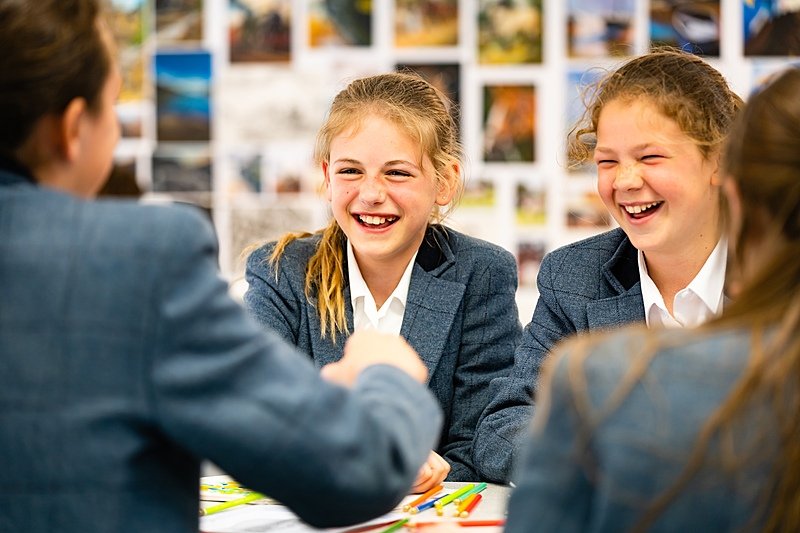 Four girls in grey school uniform sitting at a table laughing