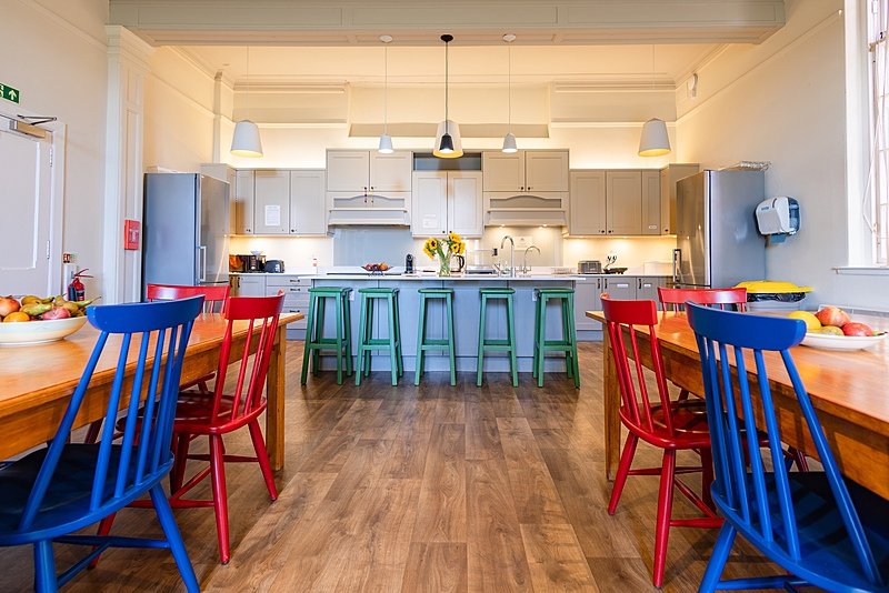 The bright kitchen in a boarding house with colorful chairs around the tables
