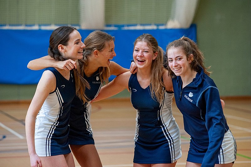 four netball girls in their school sports gear holding arms in a sports hall