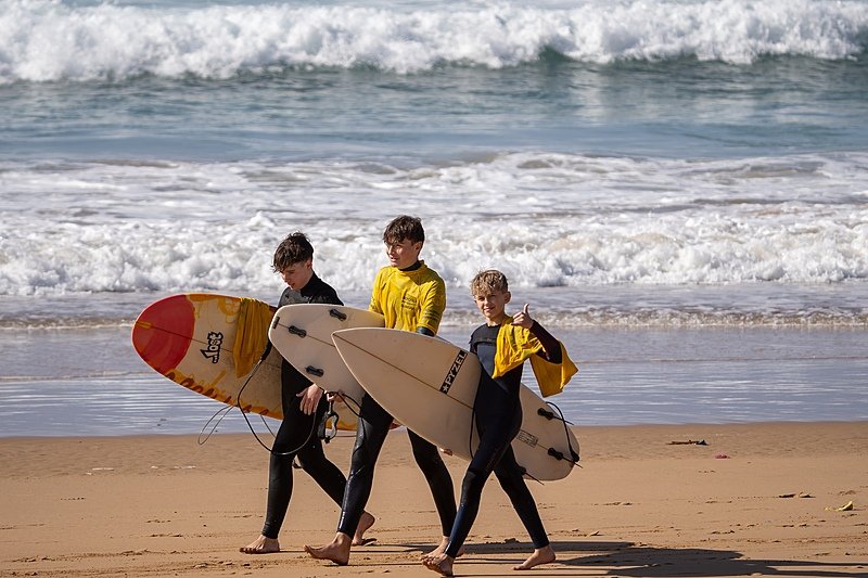 Three boys in wetsuits carrying their surfboards along the beach
