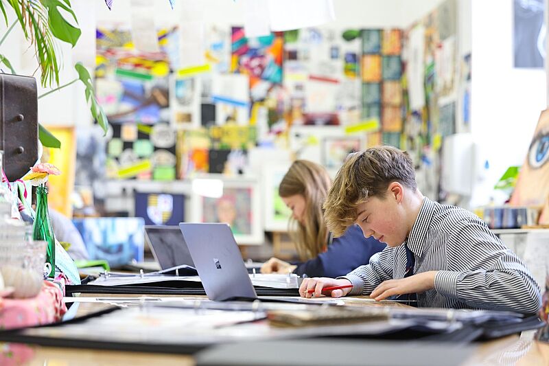 Students learning at their desks with their laptops open on the tables