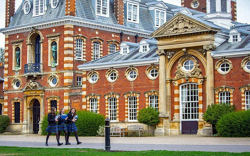 The beautiful facade of Wellington College with three students in their uniforms walking past in the foreground