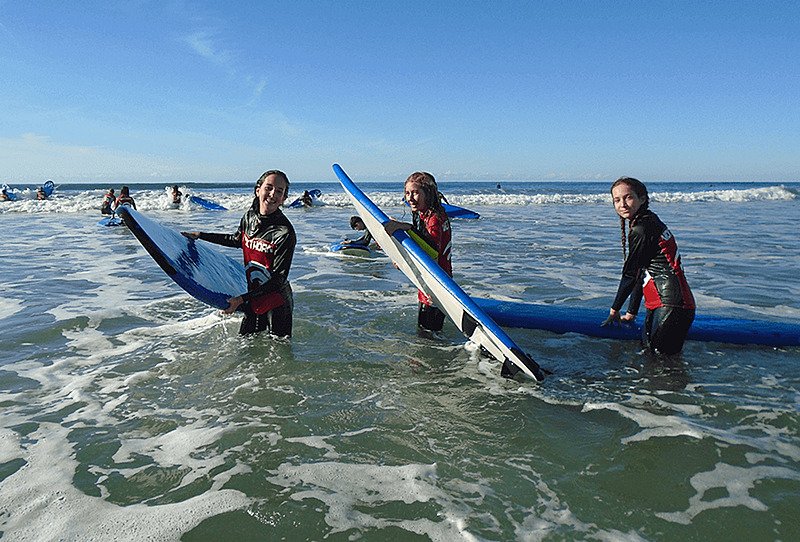 Three girls in wet suits and surf boards in the water, looking happy