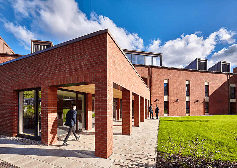 Modern red-brick building with outer corridor under which a pupil walks swiftly