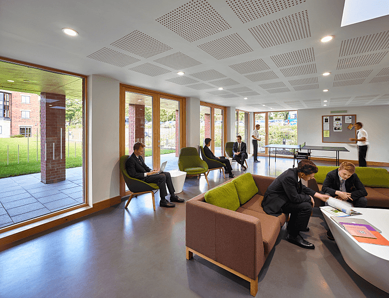 Modern, well-lit common room with pupils sitting on green chairs and borwn sofas working