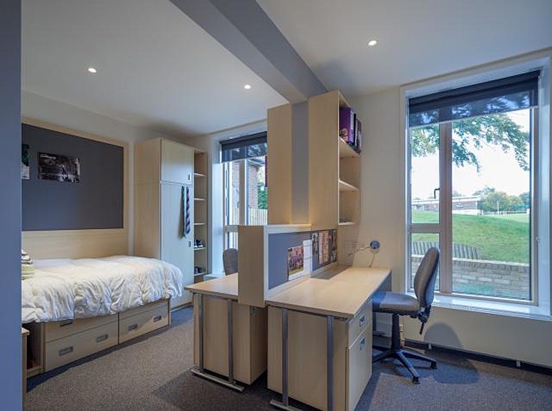 A boarding room with a bed and two tables. Very modern and roomy