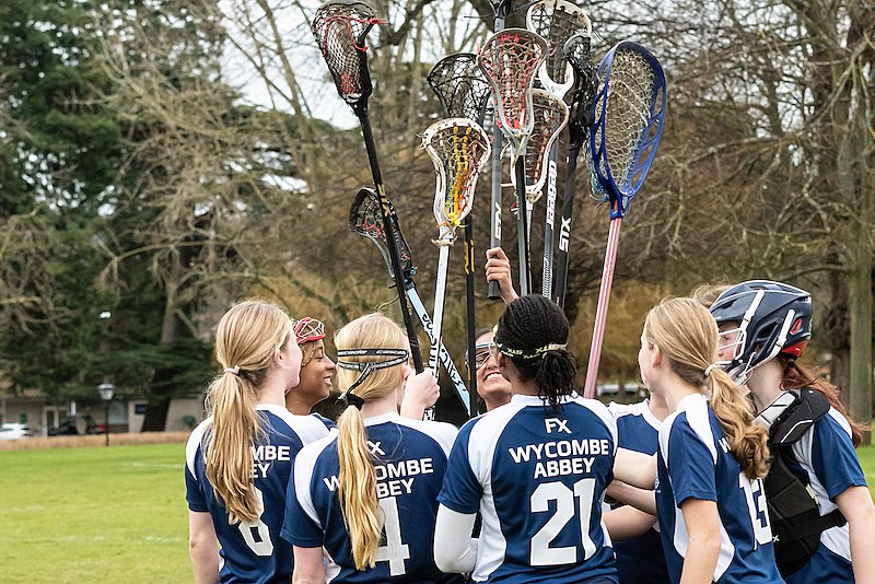 A group of girls in lacrosse gear holding up their sticks